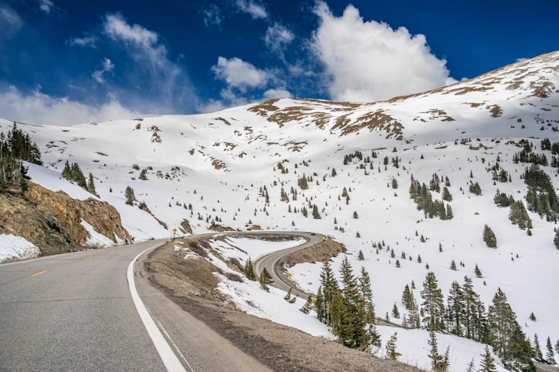 a paved road winds down beneath snowy mountains