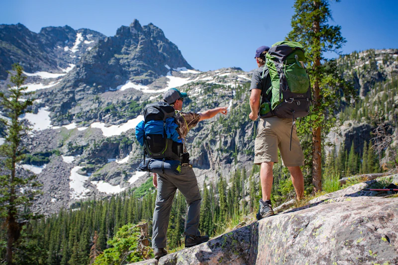 two men with large backpacks observe mountains and the forest