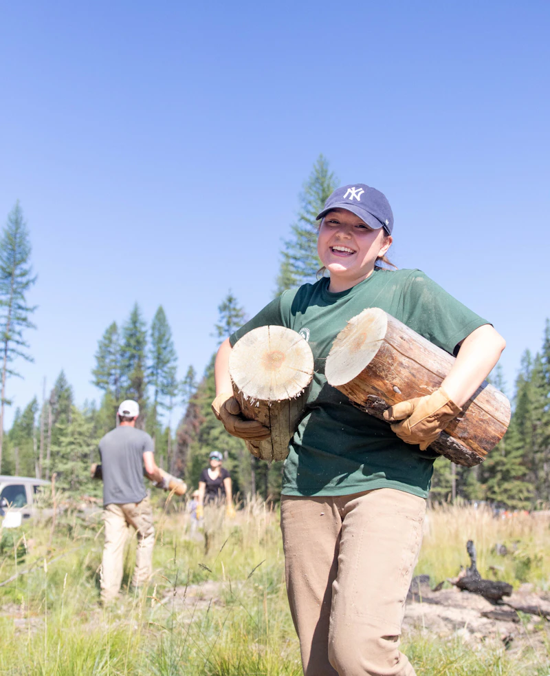 a young woman carries to large logs