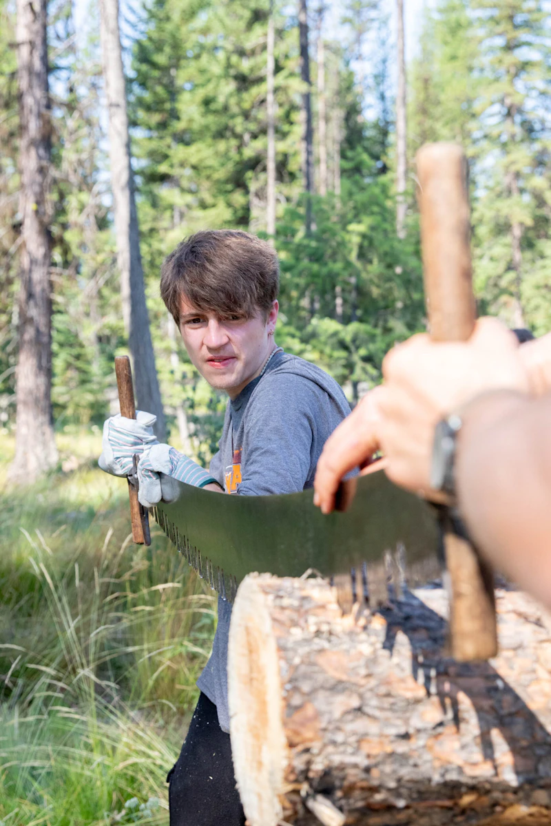 young man uses a cross cut saw