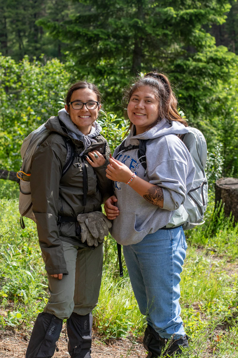 two young adults smile at the camera in the woods while doing restoration work