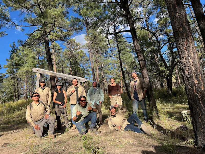 group of young adults pose for a group photo in the forest holding a cross cut saw