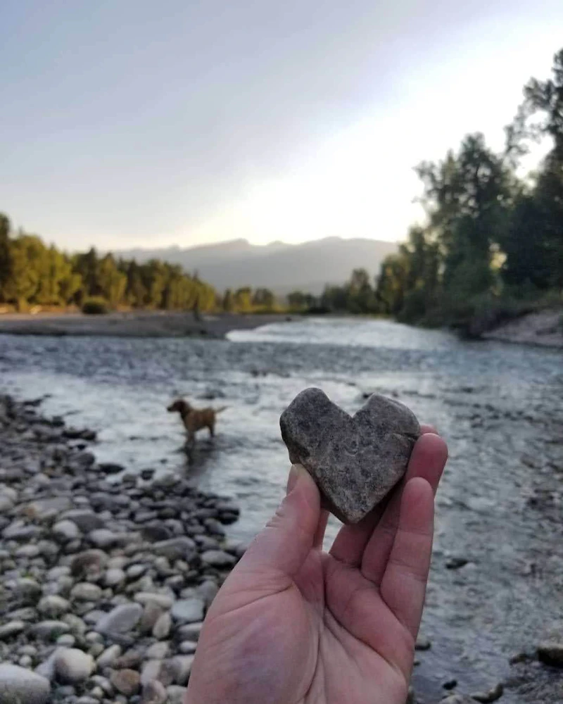 Hand holds a heart-shaped rock in front of the Bitterroot River in Montana.