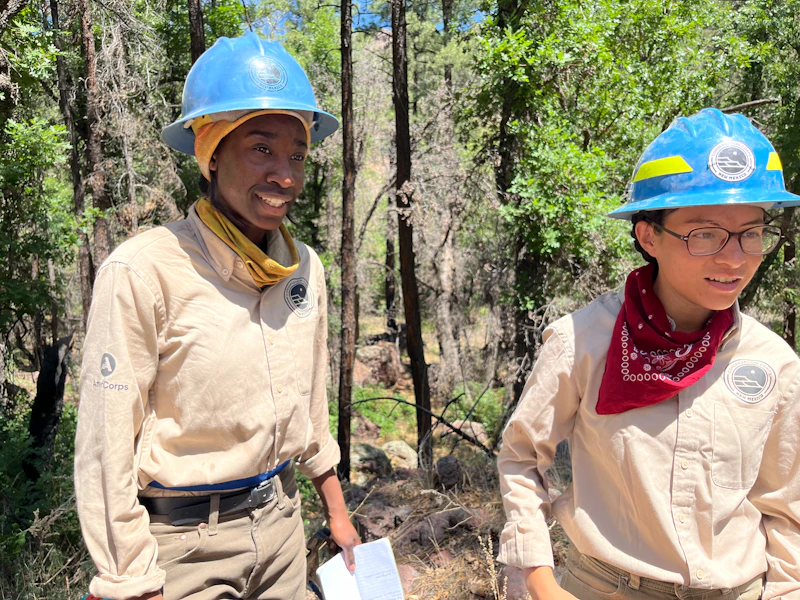 two crew members with blue hard hats stand in the forest