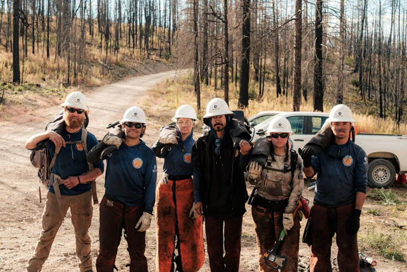 a group of young adults in hard hats in a forest road with tools to do trailwork
